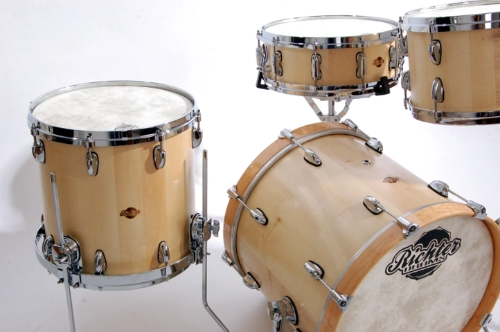 Ahorn-Schlagzeug Ahorn-Schlagzeug-Set bestehend aus einer Bassdrum, einem Floor Tom und zwei montierten Toms. Das Finish des Ahornholzes präsentiert eine feine, natürliche Maserung, die durch verchromte Hardware akzentuiert wird.