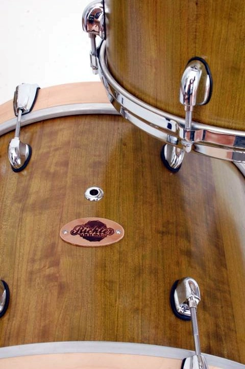 Kirschholz-Schlagzeug-Naturfinish Nahaufnahme von zwei Trommeln mit hellem Holzfinish und verchromter Hardware. Auf einer der Trommeln ist das Richter Drums-Logo sichtbar.