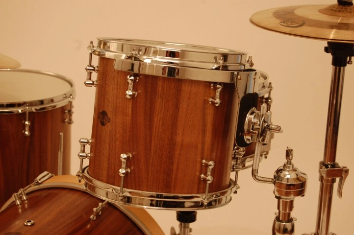 Schlagzeug-Nussbaum-richter-drums Nahaufnahme eines Tom-Toms mit warmem Holzfinish und verchromter Hardware. Das Trommelfell ist gespannt, und die Halterung mit Befestigungselementen ist gut sichtbar