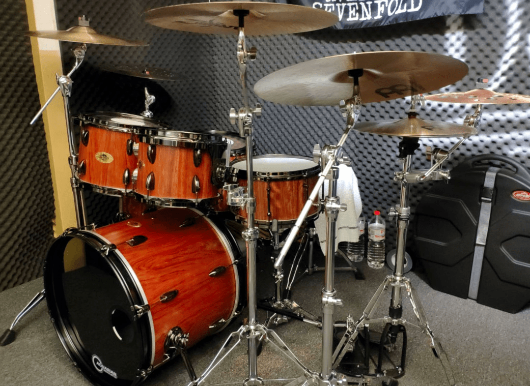 jarrahset-customdrums-1 Schlagzeug-Set aus Bubinga-Holz, bestehend aus einer Bassdrum, einem Floor Tom und zwei montierten Tom-Toms. Die Trommelkessel haben ein natürliches Holzfinish, das die warme, rötlich-braune Maserung des Bubinga-Holzes zur Geltung bringt. Verchromte Hardware sorgt für Stabilität und hochwertige Optik.